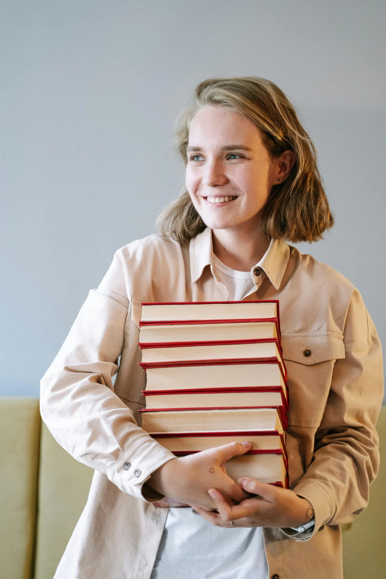 Blonde girl carrying a stack of red books in her arms, wearing a chore jacket