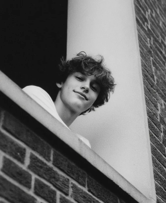 Photograph taken from below of a happy teenager who is perched on a window ledge